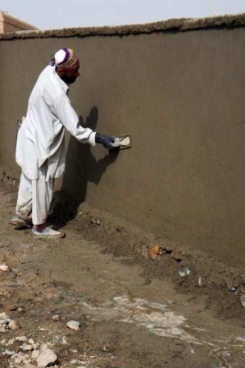 An Afghan-international security force provides security at a compouan Afghan local national worker conducts masonry work to a repair the walls of Karsai High School