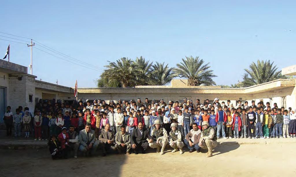 members, and the children and teachers of Karrar School stand outside of a newly renovated school.