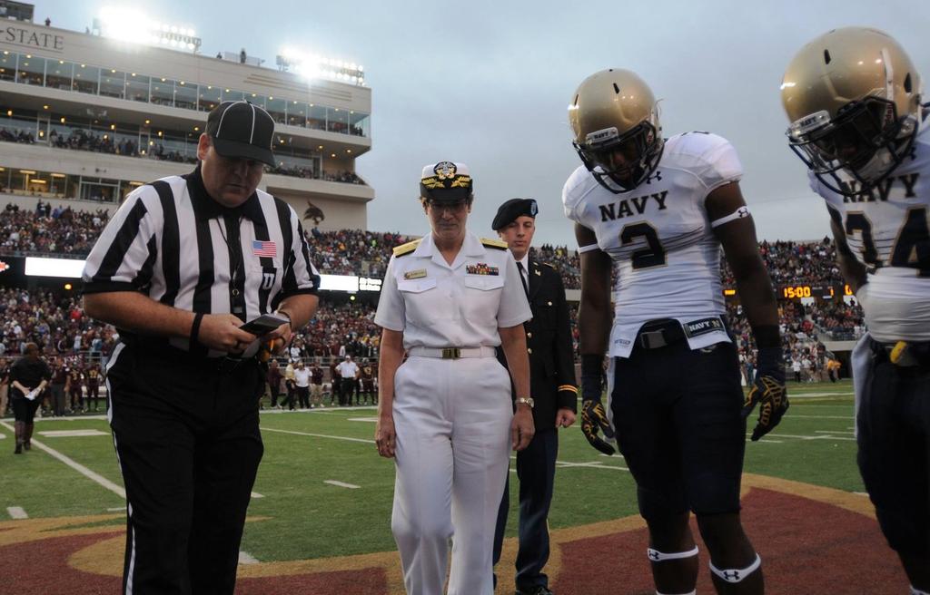 NMETC NEWS 9 LEFT: RADM Rebecca J. McCormick -Boyle with Navy football players looking down at the coin toss made by McCormick-Boyle.