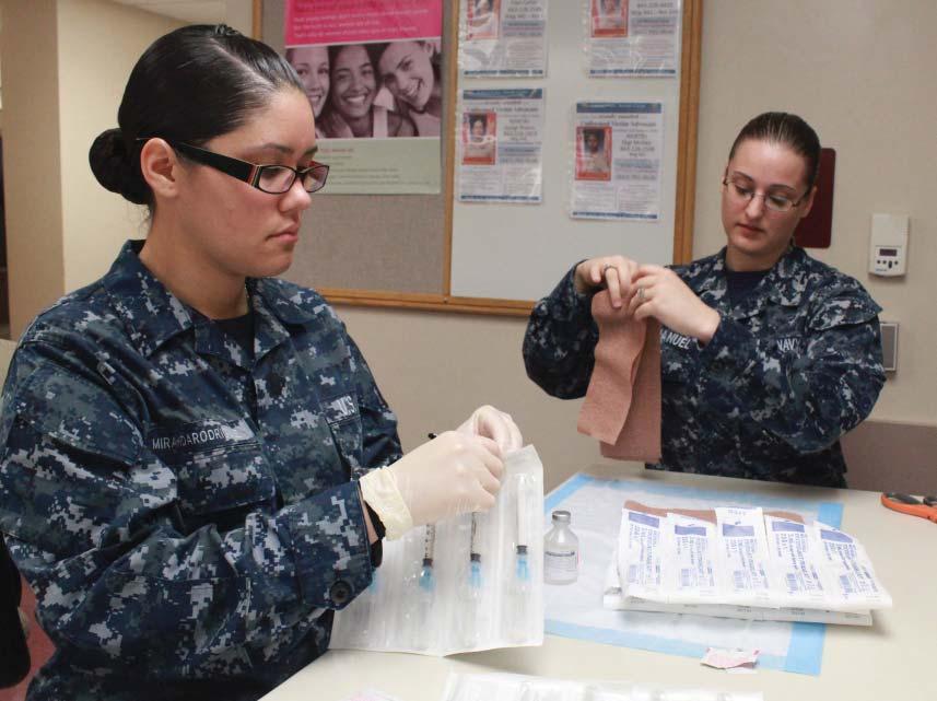 Hospitalmen Katie Manuel and Adriana Miranda-Rodriguez make preparations to assist with the insertion of contraceptive implants for female enlisted recruits at the 4th Battalion Aid Station, Marine
