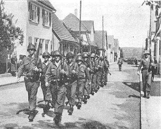 Guard detail of the 397th Infantry marches to duty, summer, 1945. Three suspected "Werwölfe" captured by the 398th Infantry in Winnenden.