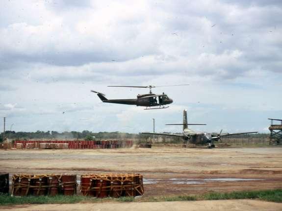 Soc Trang Army Airfield In this picture, a UH-1 Huey flies past a parked C-7 Caribou transport aircraft.