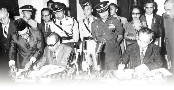 Tun Abdul Razak (left) with Dr Adam Malik (right) signing the peace treaty. Standing between them is Indonesian Army Chief, General Suharto.
