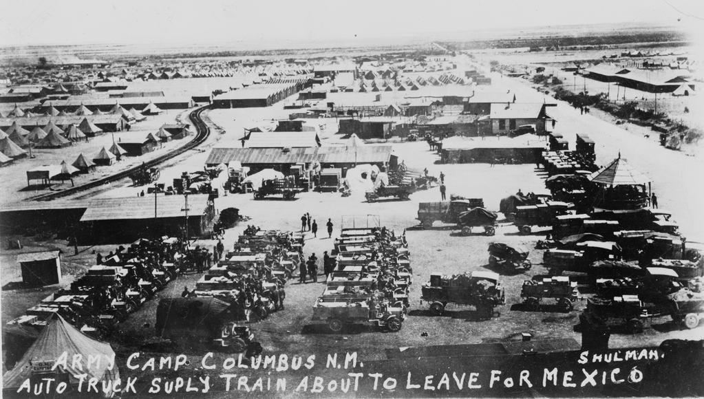 A convoy, in the foreground, lines up before departure. In the background, supply support activities and troop billets fill the countryside near Columbus, New Mexico.