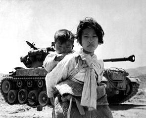 Photograph captioned With her brother on her back a war weary Korean girl tiredly trudges by a stalled M-26 tank, at Haegju, Korea, 6/9/1951.