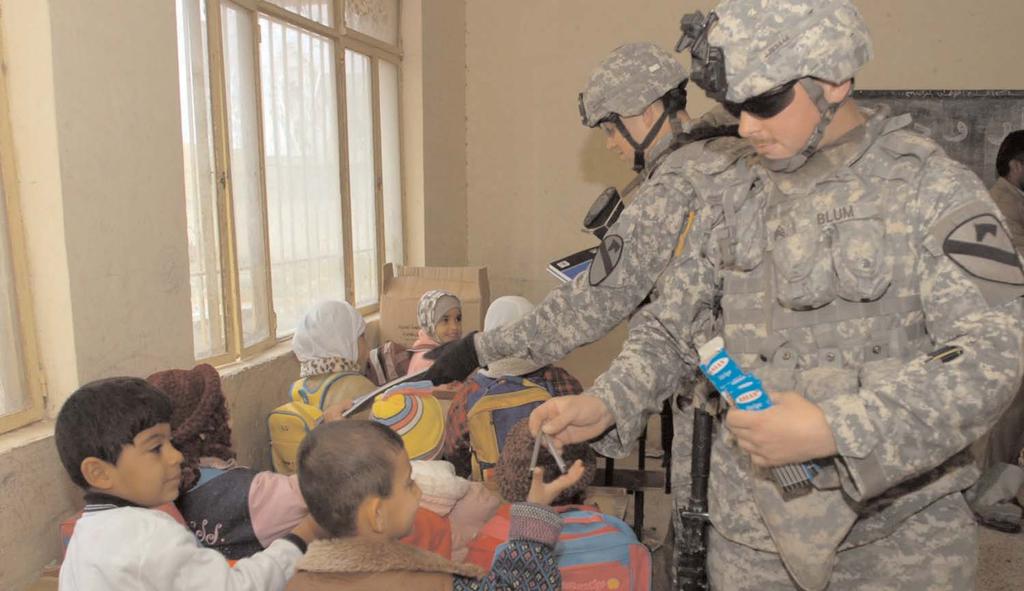 Daniel Slotemaker, an infantryman, both from Troop B, 1st Squadron, 7th Cavalry Regiment, hand out school supplies to students at the Al Balkess Primary School in Saab Al Bour, Iraq.