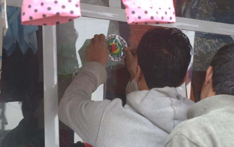 An Afghan man places a sticker in the window shop that he received from American soldiers saying "Everyone is doing their part for Afghanistan" at the top and on the bottom it says "I am