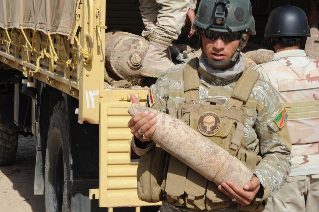 Iraqi soldiers with the Bomb Disposal Company, 9th Iraqi Army Disposal unload three trucks of unexploded ordinances, supervised by U.S.