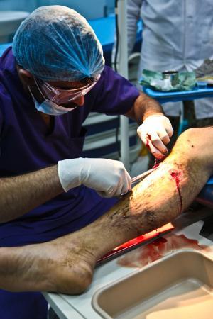 An Afghan National Army doctor of the Paktia Regional Military Hospital, 203rd Corps, stitches a patients wounded leg caused by an improvised explosive device at Forward Operating Base Thunder,