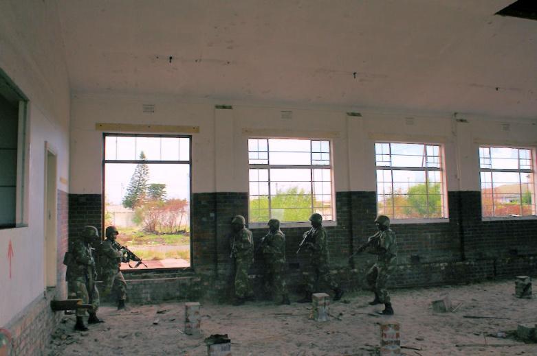 A small group of soldiers in full kit, their R4 assault rifles at the ready, sprinted across an open patch of ground, eager to reach the shelter of the wall at the base of the control tower.