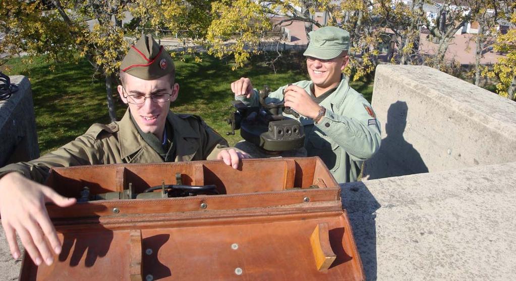In this photo, PVT Rosamilia and CPL Minton install an M1910A1 azimuth instrument and telescope on the pedestal inside the Battery Commander s