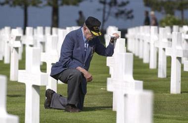 WWII and D-Day veteran Raymond Moon kneels before the grave of a fallen comrade at the American