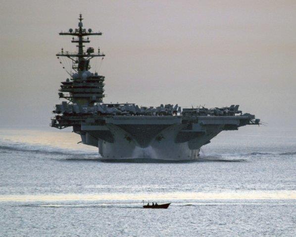 A small vessel transits in front of the Nimitz-class aircraft carrier USS George H W Bush (CVN 77) as it transits the Strait of Hormuz on 28 April 2014.