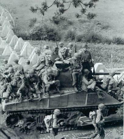 Infantrymen riding on a M4 medium Sherman tank-dozer pass through the Siegfried Line in early October 1944. The division continued to attack, defeating several German counter-attacks in the process.